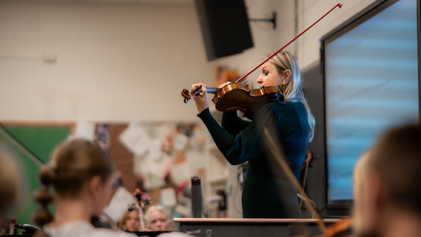 An orchestra instructor playing a viola in front of her class of students