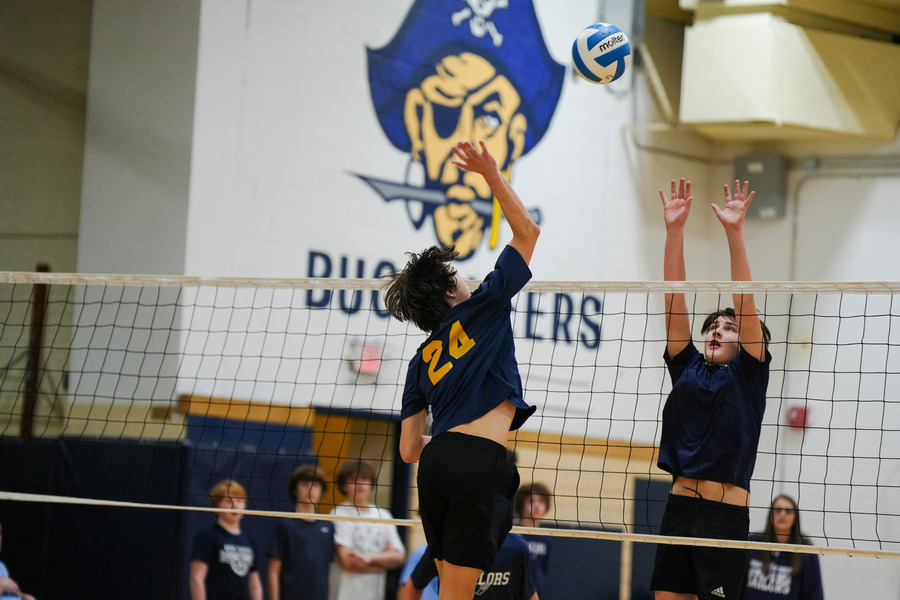 A Lakeshore Middle School male athlete jumping up to spike a volleyball over the net toward a defender who is attempting to block the shot.